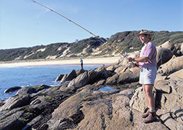 A man standing on rocks fishing in the ocean at Salmon Rocks Cape Conran.