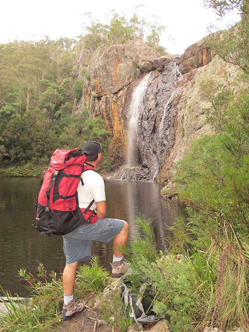 A man with backpack looking at waterfall, Raymond Creek Falls, Orbost Region.